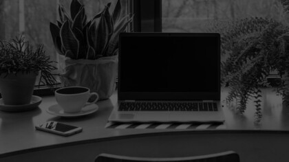 a laptop, plant, phone and cup of coffee sitting on a disk